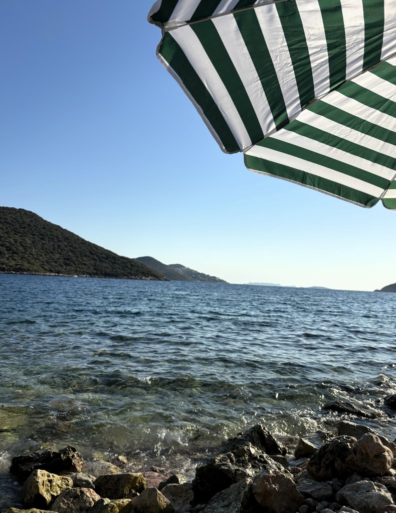 Şemsiye altında deniz manzarası ve kayalık kıyı.